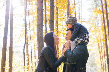 People, family and leisure concept - happy father holding little daughter on back in autumn park and mother