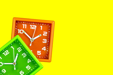 Two bright alarm clocks on a yellow background. Table clock green and orange.