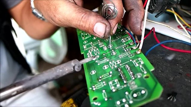 Close up video of the hands of an electrician fixing or soldering an electronic circuit board.