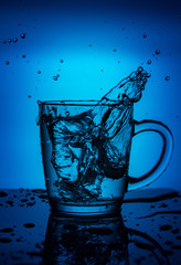 Splash of water in a cup on a blue background.