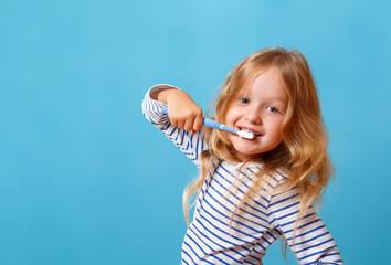 A little girl in striped pajamas is brushing her teeth with a toothbrush. The concept of daily...