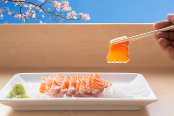 Close up,Hand holding salmon sashimi using chopsticks - Raw fresh salmon sliced served on white...