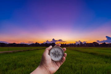 A man holding compass on hand at field and sunset for navigation guide. © tortoon