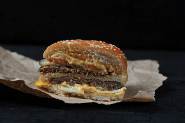 fast food - cut in half Burger with cheese and beef on Kraft paper on black charcoal background