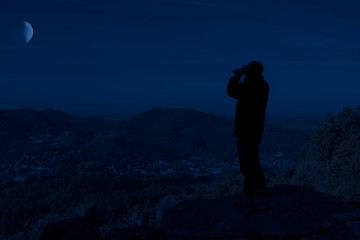 Silhouette von einem Mann wo auf einem Berg mit Fernglas steht