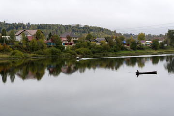 village on the bank of the autumn river in cloudy weather, in the middle of the river you can see a boat with a fisherman