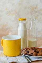 Yellow mug with milk, cookies and milk bottles on the background - shallow depth of field.