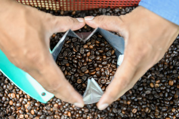 Coffee beans in bag with hand holding bag.