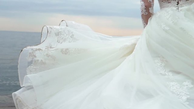 The beautiful blonde bride on a walk by the sea circling and waving dress slowmotion at cloudy day