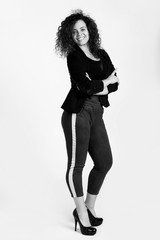 Beautiful woman with a dazzling open smile and a lush hairdo in Afro-style poses on a white background. The woman is dressed eclectically in leggings and a shortened jacket. Black and white photo. 