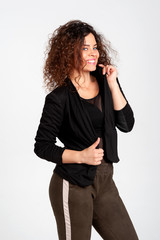 Beautiful woman with dazzling open smile and lush hairdo in afro style posing on white background. The woman is dressed eclectically in khaki leggings and a shortened jacket. 