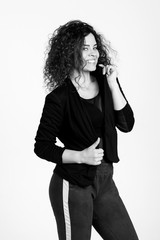 Beautiful woman with a dazzling open smile and a lush hairdo in Afro-style poses on a white background. The woman is dressed eclectically in leggings and a shortened jacket. Black and white photo. 