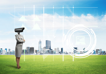 Camera headed woman standing on green grass against modern cityscape