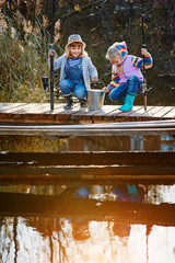 Two little girls with fishing rods, sitting on a wooden pontoon and bragging of caught fish