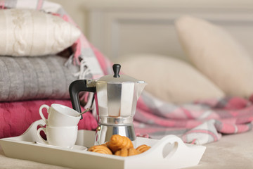 Breakfast in bed. On a white wicker tray there is a coffee maker, coffee cups and croissants.