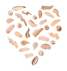 Creative set with different makeup product smears in shape of heart on white background