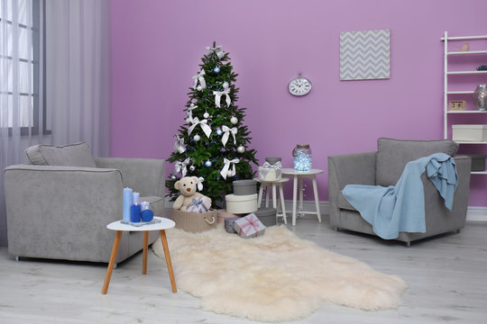 Stylish Christmas interior with fir tree and comfortable armchairs near color wall