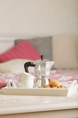 Breakfast in bed. On a white wicker tray there is a coffee maker, coffee cups and croissants.