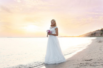 Fototapeta na wymiar Happy bride holding wedding bouquet on beach at sunset