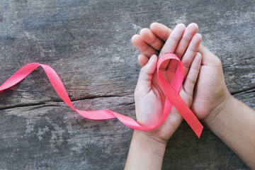hand holding pink ribbon on wood.  breast cancer awareness. concept healthcare and medicine
