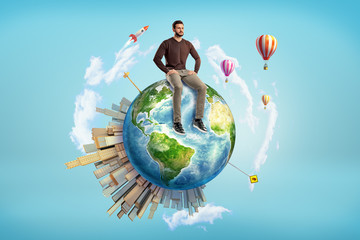 A bearded man sits on a small Earth globe with skyscrapers on its surface and hot air balloons...