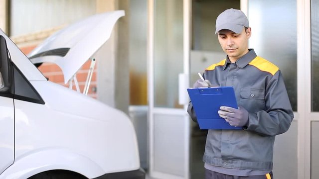 Mechanic writing documents with a truck in the background