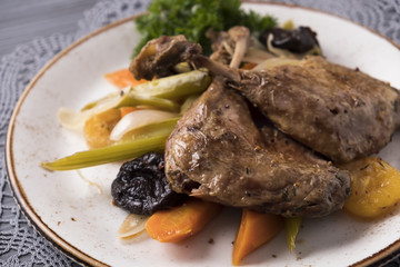 Delicious roasted duck legs with vegetables, prunes and dried apricots. Closeup