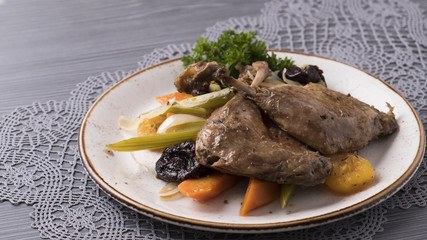 Duck legs with vegetables, prunes and dried apricots on a plate.