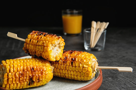 Plate with delicious grilled corn cobs on gray table against black background