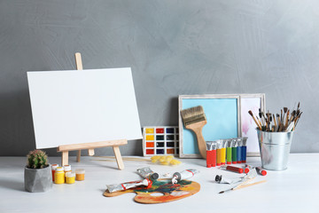 Easel with space for design and set of professional art supplies on table against grey background