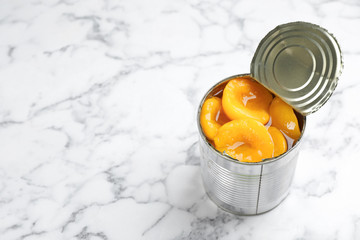 Tin can with conserved peach halves on marble background. Space for text