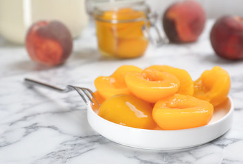 Plate with conserved peach halves on marble table