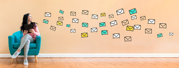 Many emails with young woman holding a tablet computer in a chair