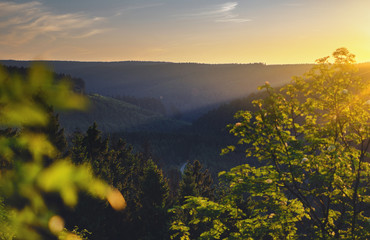 View from a mountain top with sunset sun rays in the valley and colorful fresh green trees. Oker Dam (Okertalperre), mountain landscape in National Park Harz, Goslar, Bad Harzburg in Germany