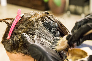 Closeup of hair dresser applying chemical color dye onto hair