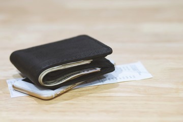 Money and credit card in a leather wallet on wooden table with mobile smart phone and bill slip paper background. shopping online.  finance  Expenses charges concept