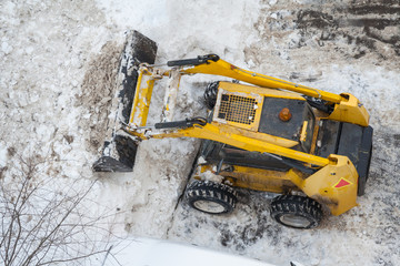 Top view of a snow-removing machine shoveling the snow on a dirty road