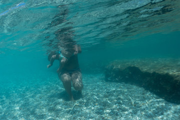 Mother holds a small baby with a diaper and teaches him to swim in the sea. underwater photo