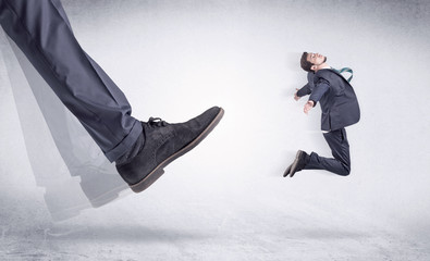 Boss mobbing his worker, illustrated by black shoe kicking small businessman who is flying away in...