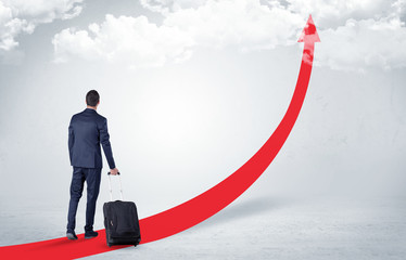 Obraz premium Young businessman with back leaving on the red arrow carpet to the skies with luggage on his hand 