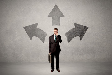 Charming businessman in doubt, choosing from three directions in front of a grey wall
