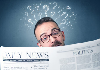 Young confused businessman reading daily newspaper with question marks above his head