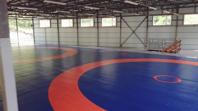 A large gym for wrestling without people with mats and blue color covered with orange markings. A carpet for martial arts called tatami