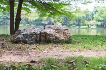 Big stone in a park with green trees, large ponds