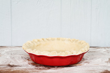 Homemade butter pie crust in pie plate with fluted pinched edge against a rustic wooden background. Crust is empty and ready for baking.
