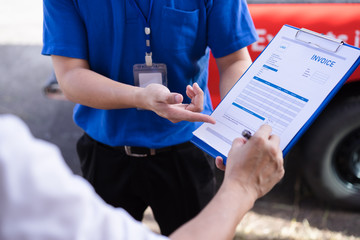 Young man signing invoice bill from delivery man after receiving parcel from courier at home. Delivery service concept