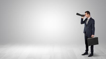 Businessman looking forward with binoculars in an empty space
