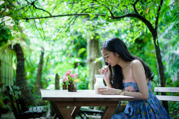 Asian pretty girl has drinkling ice white milk with happy and smiling at Little Tree Garden cafe, Nakhon Pathom province, Thailand in the morning.