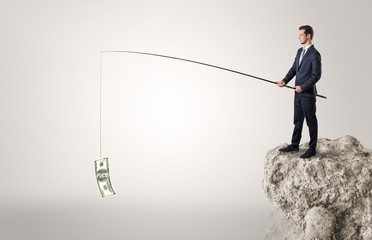 Elegant young businessman fishing cash from a huge rock