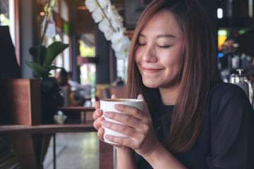 Closeup image of Asian woman close her eyes to smelling and drinking hot coffee with feeling good in cafe